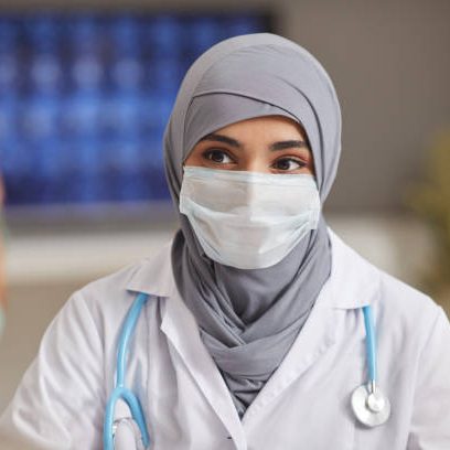 Portrait of muslim doctor in protective mask looking at her patient while they sitting at hospital